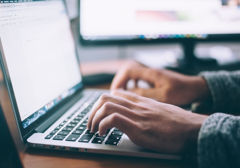 Hands typing on a laptop beside a monitor